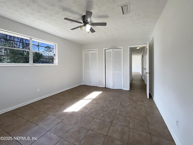 unfurnished bedroom featuring multiple closets, visible vents, a textured ceiling, dark tile patterned flooring, and baseboards