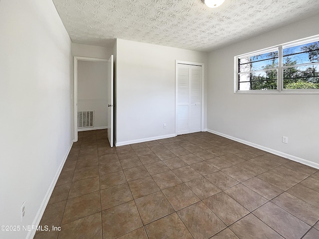 unfurnished bedroom with a closet, visible vents, a textured ceiling, and baseboards