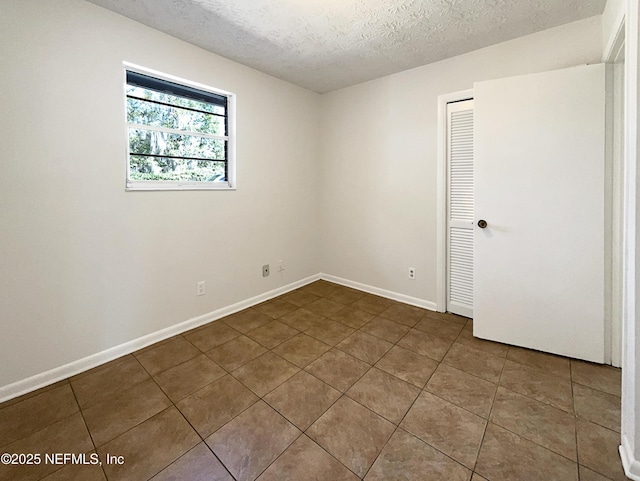 tiled empty room featuring a textured ceiling and baseboards