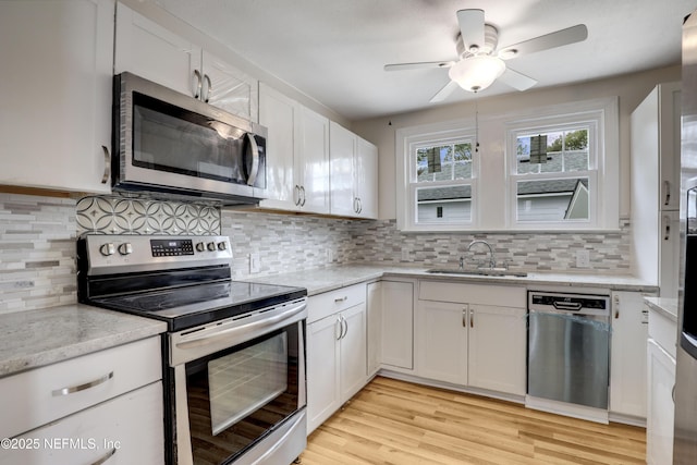 kitchen with sink, light stone counters, white cabinetry, light hardwood / wood-style floors, and stainless steel appliances