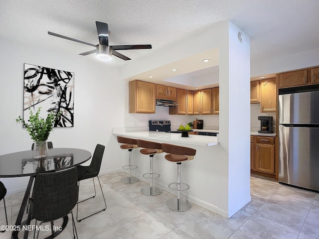 kitchen featuring a textured ceiling, range with electric stovetop, stainless steel refrigerator, a kitchen breakfast bar, and kitchen peninsula