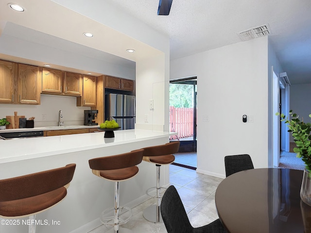 kitchen with a breakfast bar, stainless steel refrigerator, sink, light tile patterned floors, and a textured ceiling