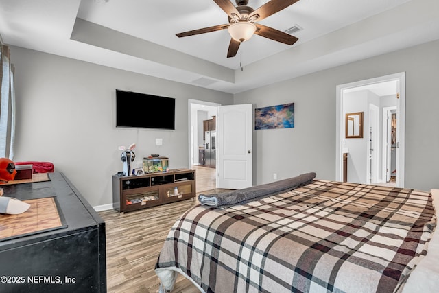 bedroom featuring a tray ceiling, ensuite bathroom, ceiling fan, and light wood-type flooring