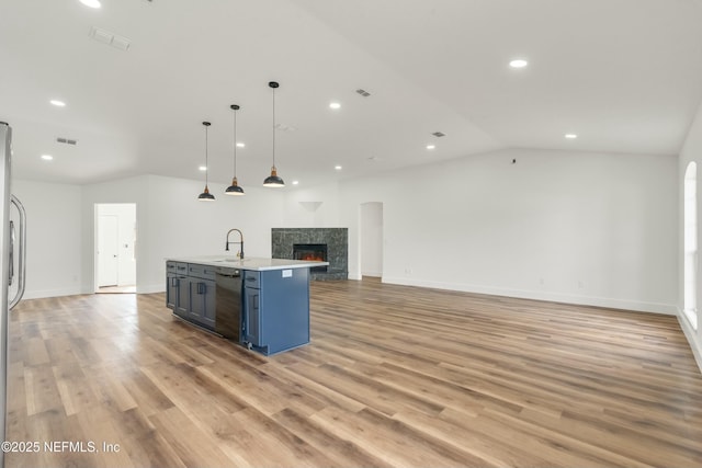 kitchen featuring dishwasher, an island with sink, sink, a tiled fireplace, and hanging light fixtures