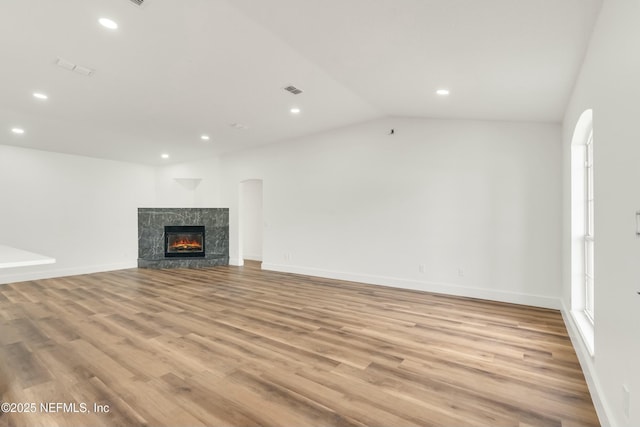 unfurnished living room with vaulted ceiling, light wood-type flooring, a high end fireplace, and a healthy amount of sunlight