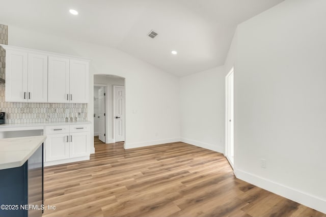 kitchen with backsplash, light hardwood / wood-style flooring, white cabinets, and vaulted ceiling