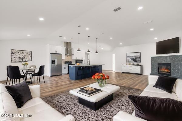 living room with lofted ceiling, light wood-type flooring, sink, and a high end fireplace