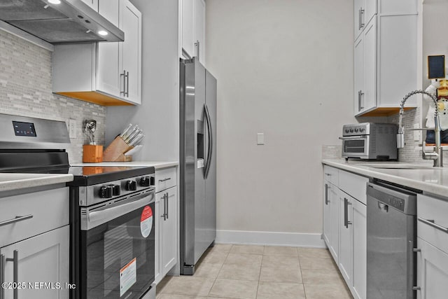 kitchen with light tile patterned floors, appliances with stainless steel finishes, white cabinetry, backsplash, and range hood