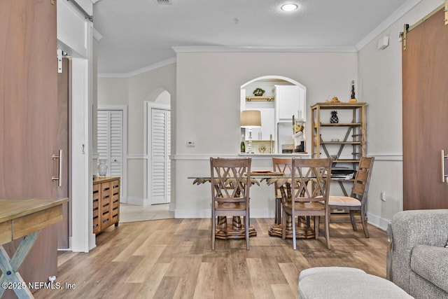 dining area featuring crown molding, a barn door, and light hardwood / wood-style flooring