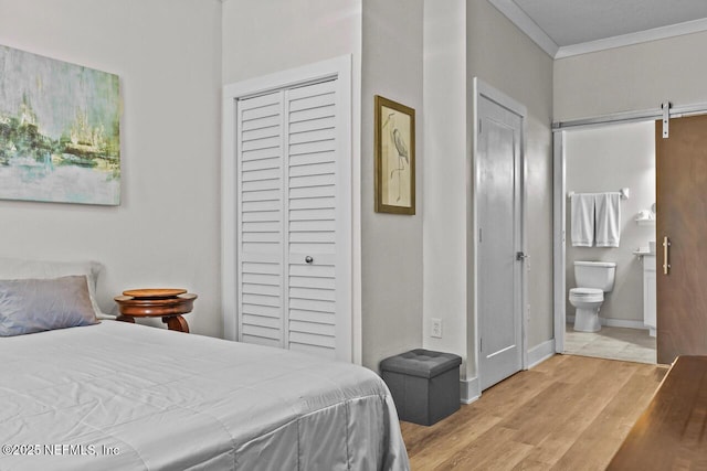 bedroom with crown molding, connected bathroom, a barn door, and light hardwood / wood-style floors