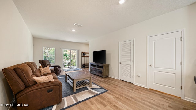 living area featuring a textured ceiling, baseboards, visible vents, and light wood-style floors