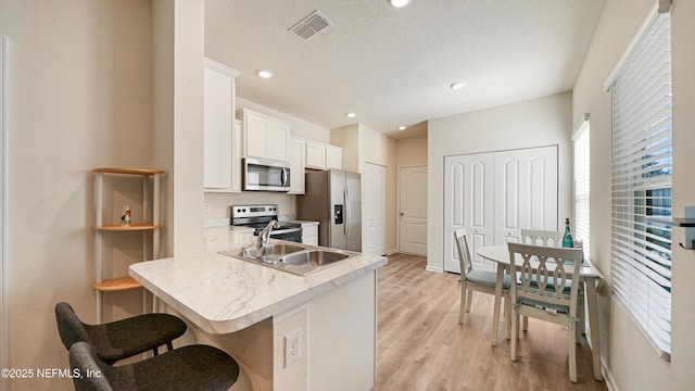 kitchen featuring visible vents, light wood-style flooring, appliances with stainless steel finishes, a kitchen bar, and white cabinetry