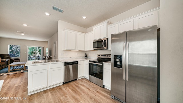 kitchen with light wood-style flooring, open floor plan, a peninsula, stainless steel appliances, and white cabinetry