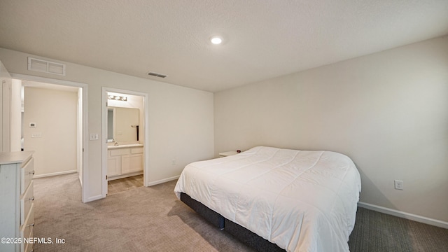 bedroom with light colored carpet, visible vents, connected bathroom, a textured ceiling, and baseboards