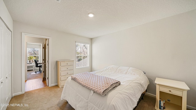 bedroom featuring a textured ceiling, a closet, baseboards, and light colored carpet