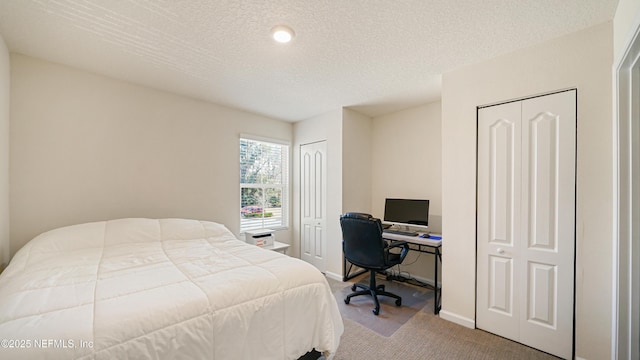 bedroom with two closets, a textured ceiling, baseboards, and carpet flooring