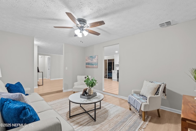 living room featuring ceiling fan, light hardwood / wood-style floors, and a textured ceiling