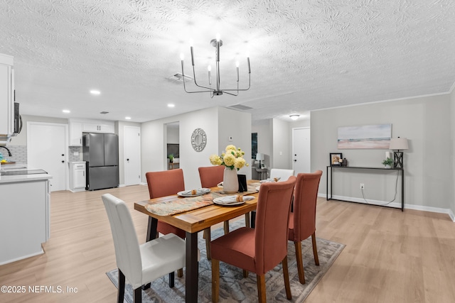 dining space with a notable chandelier, a textured ceiling, and light hardwood / wood-style flooring