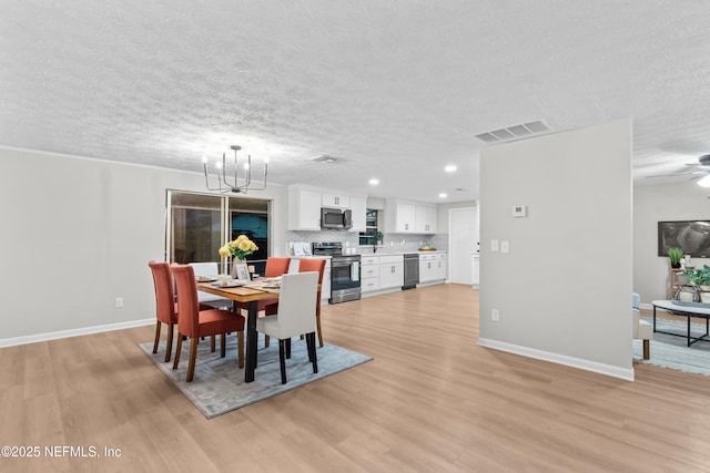 dining room with ceiling fan with notable chandelier, light hardwood / wood-style flooring, and a textured ceiling