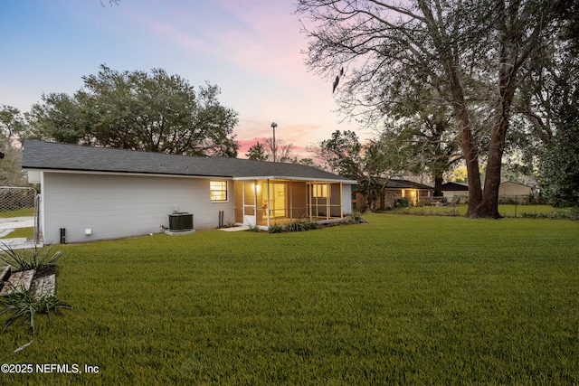 back house at dusk featuring a yard, central AC unit, and a sunroom