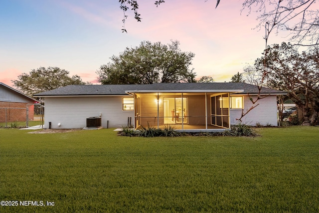 back house at dusk featuring a lawn, a sunroom, and central air condition unit