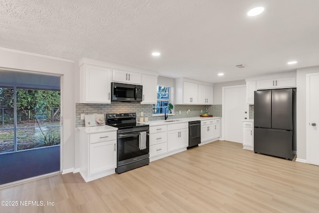 kitchen featuring sink, white cabinets, light hardwood / wood-style floors, and black appliances