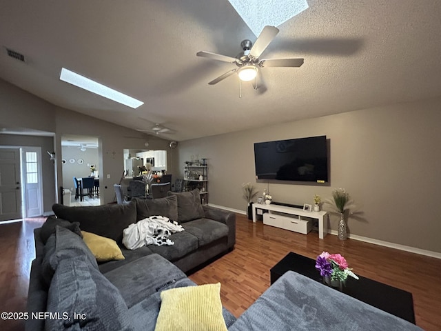 living room with wood-type flooring, vaulted ceiling with skylight, a textured ceiling, and ceiling fan