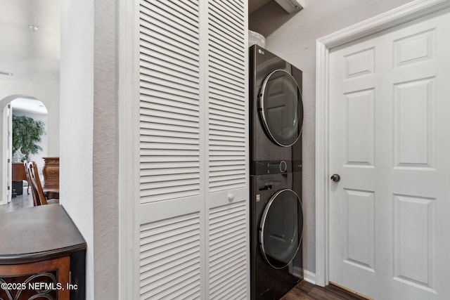 clothes washing area featuring arched walkways, a textured wall, laundry area, stacked washer / dryer, and dark wood-style flooring