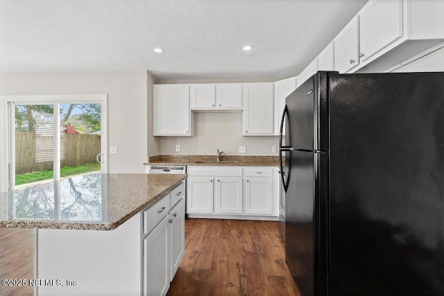 kitchen featuring sink, wood-type flooring, black refrigerator, light stone countertops, and white cabinets