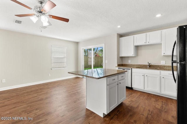 kitchen with a kitchen island, black refrigerator, dark stone countertops, white cabinets, and stainless steel dishwasher