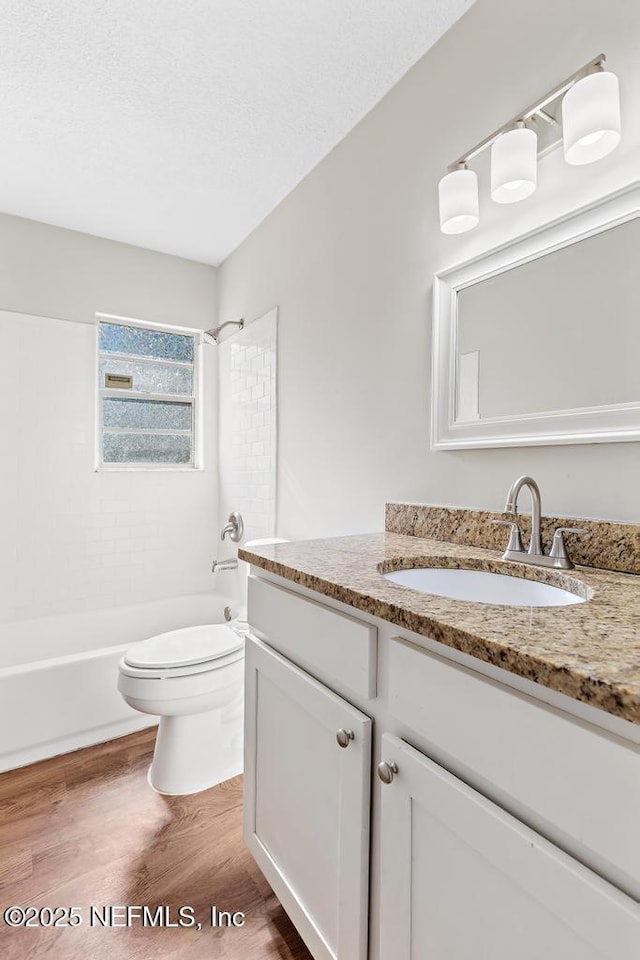 full bathroom featuring toilet, wood-type flooring, a textured ceiling, vanity, and tiled shower / bath combo