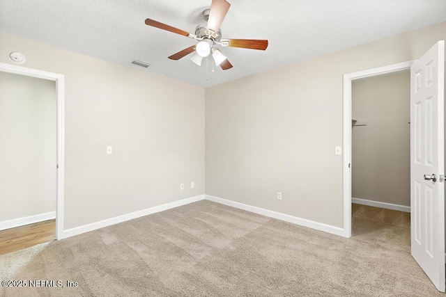 unfurnished bedroom with ceiling fan, a walk in closet, light colored carpet, and a closet