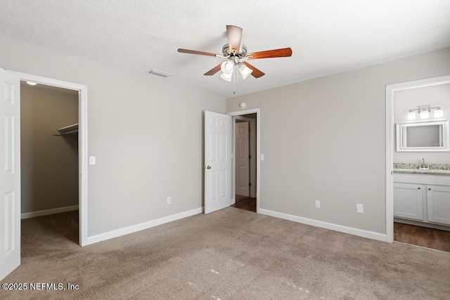 unfurnished bedroom with a walk in closet, sink, and light colored carpet