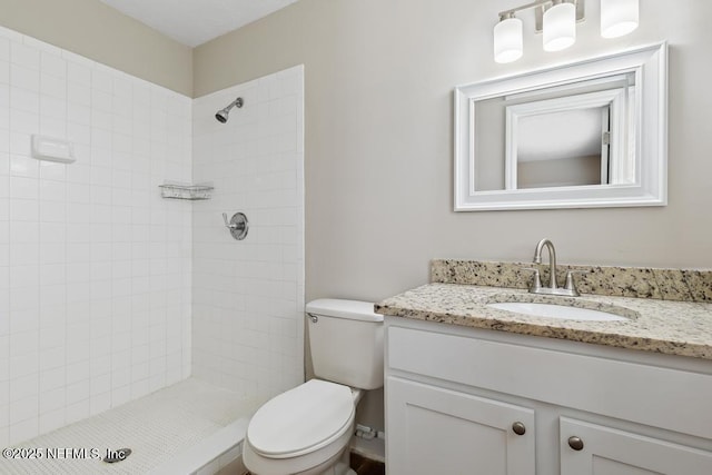 bathroom featuring vanity, a tile shower, and toilet