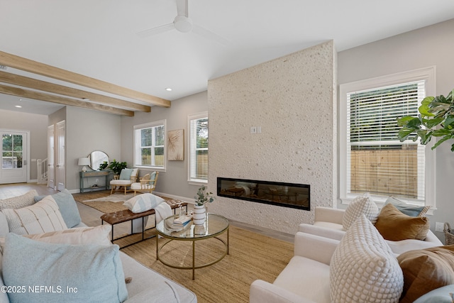 living room with ceiling fan, a large fireplace, a healthy amount of sunlight, and vaulted ceiling with beams