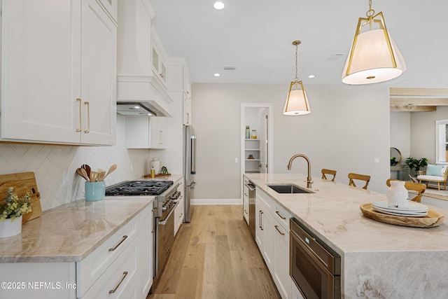 kitchen featuring stainless steel appliances, sink, white cabinets, and decorative light fixtures