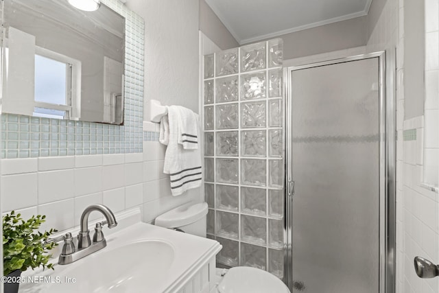 bathroom with a shower with shower door, tile walls, vanity, toilet, and crown molding