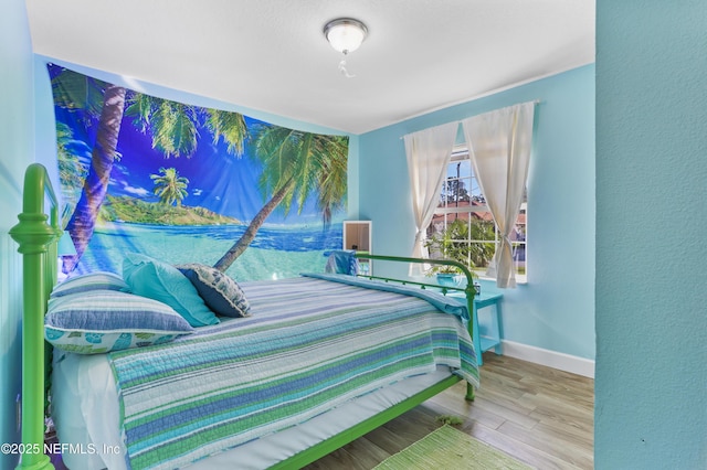 bedroom featuring a textured wall, wood finished floors, and baseboards