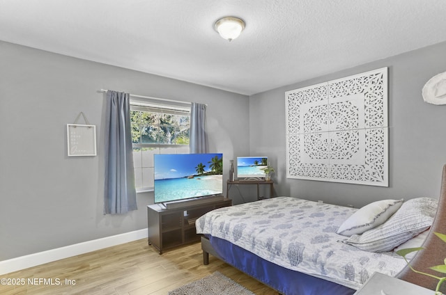 bedroom with a textured ceiling, baseboards, and wood finished floors