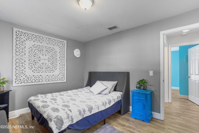 bedroom with visible vents, light wood-style flooring, baseboards, and a textured ceiling