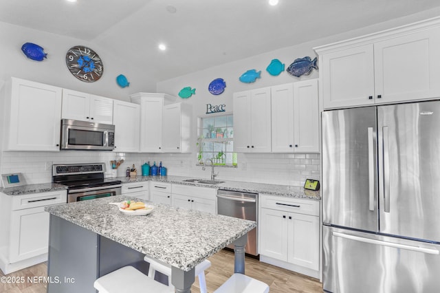 kitchen featuring light stone counters, a breakfast bar area, stainless steel appliances, a sink, and a center island