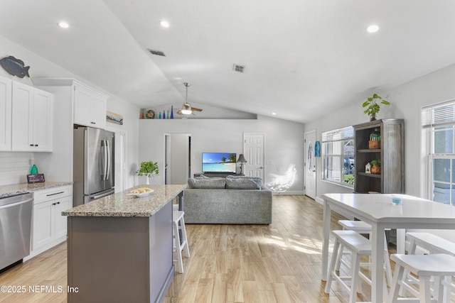 kitchen with a center island, a breakfast bar area, stainless steel appliances, open floor plan, and white cabinetry