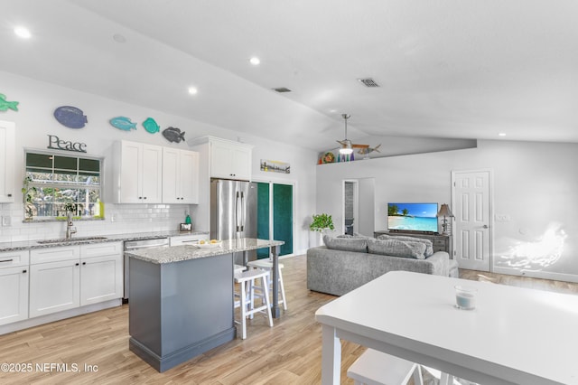 kitchen featuring white cabinets, light stone counters, a center island, freestanding refrigerator, and a sink