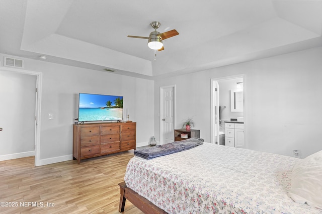 bedroom with connected bathroom, visible vents, baseboards, light wood-style floors, and a tray ceiling