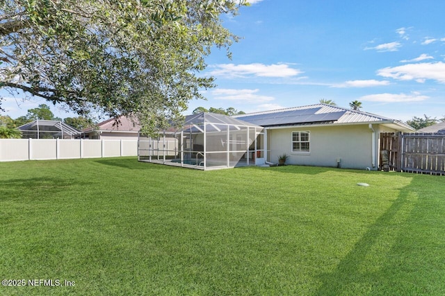 back of house with a lanai, a fenced backyard, a yard, and roof mounted solar panels