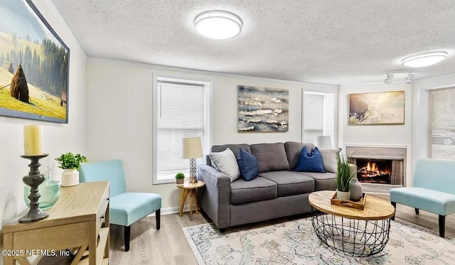 living room with a textured ceiling, light wood-style flooring, baseboards, and a lit fireplace