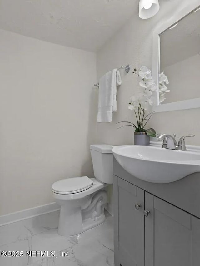 half bathroom with marble finish floor, toilet, vanity, and baseboards