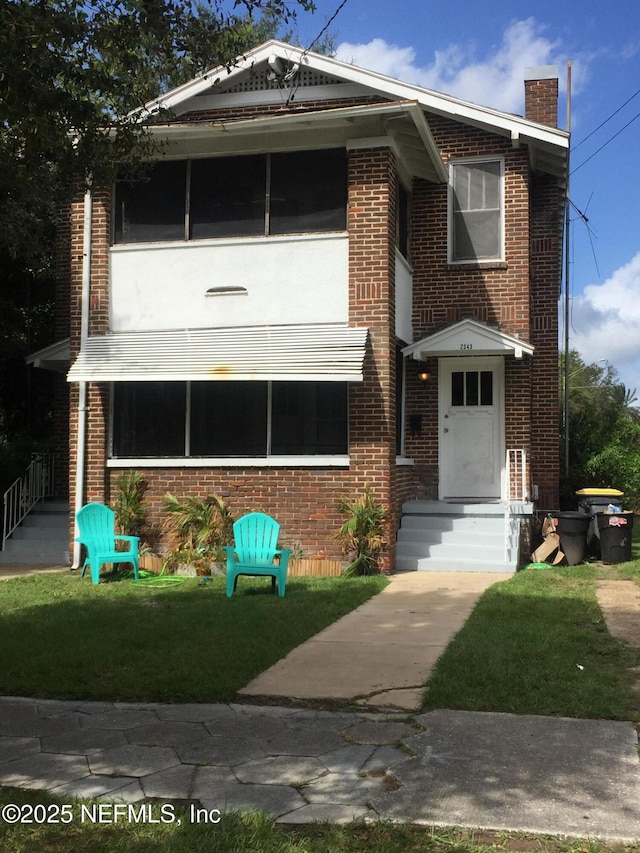 view of front of house with entry steps, a front yard, and brick siding