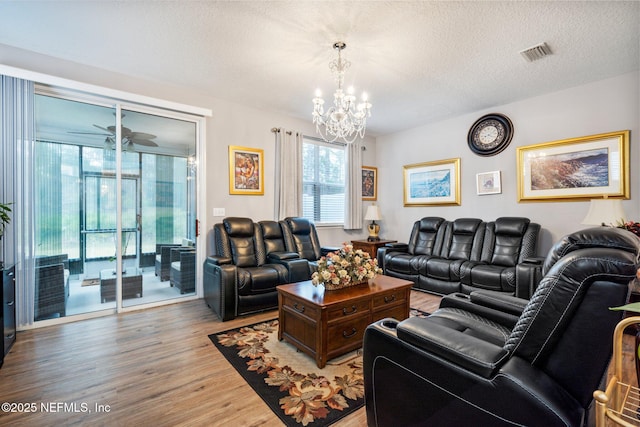 living room with a textured ceiling, light wood-type flooring, visible vents, and an inviting chandelier