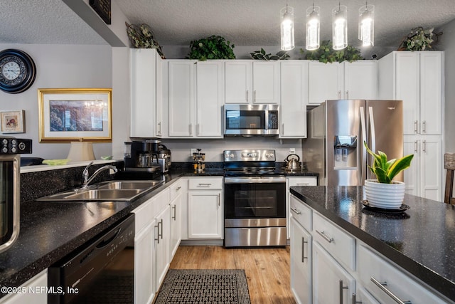 kitchen with light wood-style flooring, stainless steel appliances, a textured ceiling, white cabinetry, and a sink